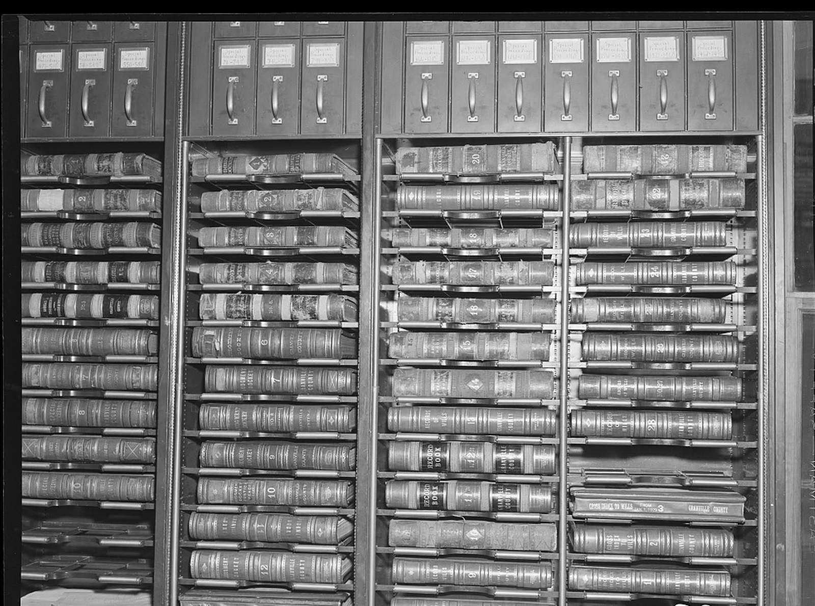 Shelves of large leather-bound record books and labeled file drawers in a courthouse records vault.